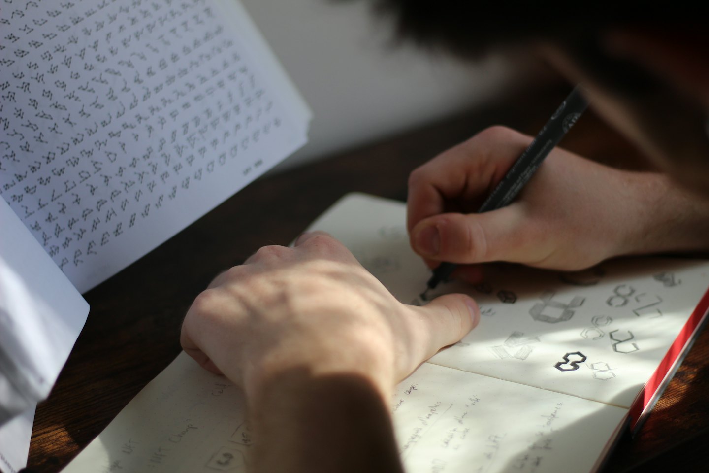 Hands sketching logo designs in a notebook with a pen.