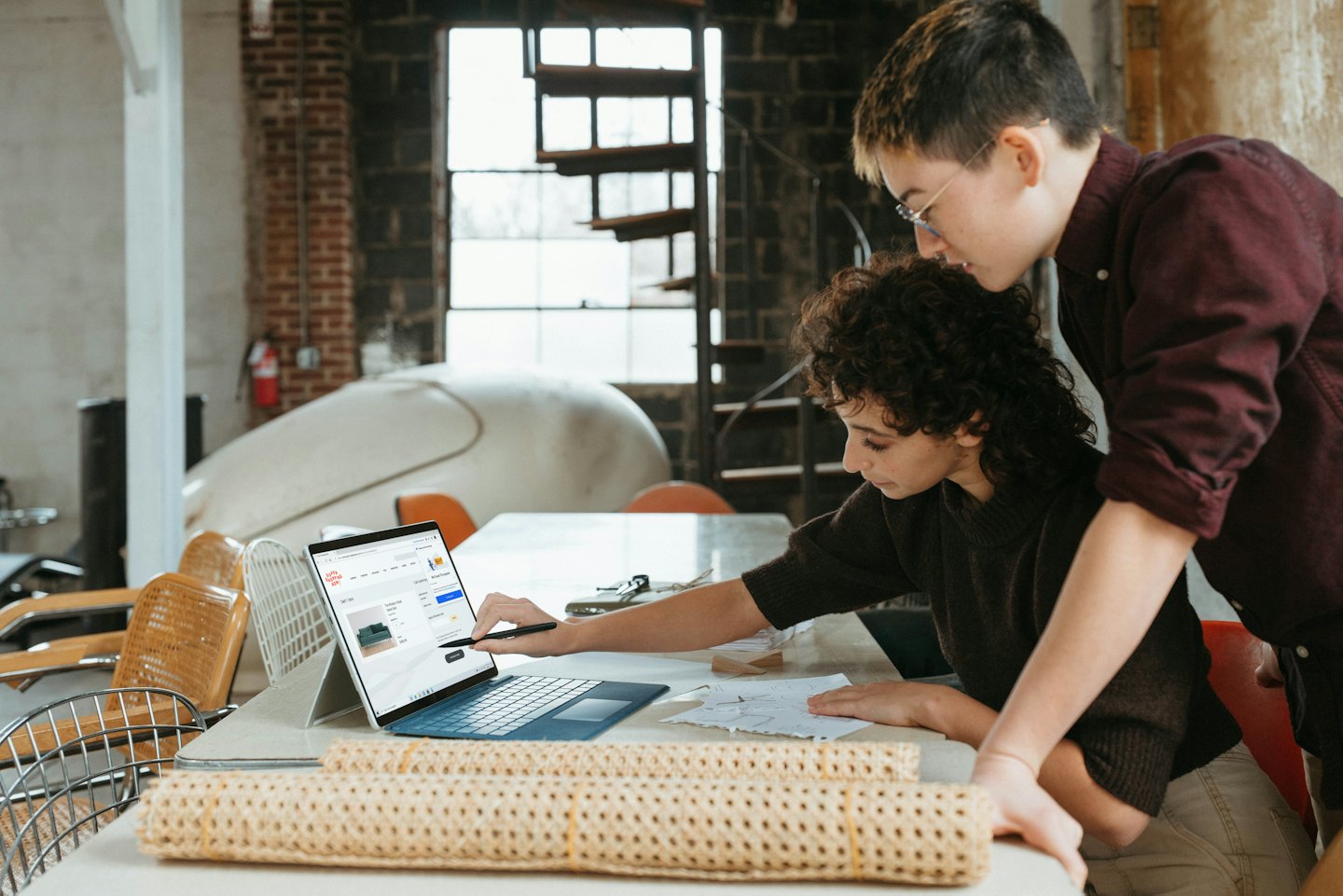 Two designers collaborate on laptop with product images on screen.