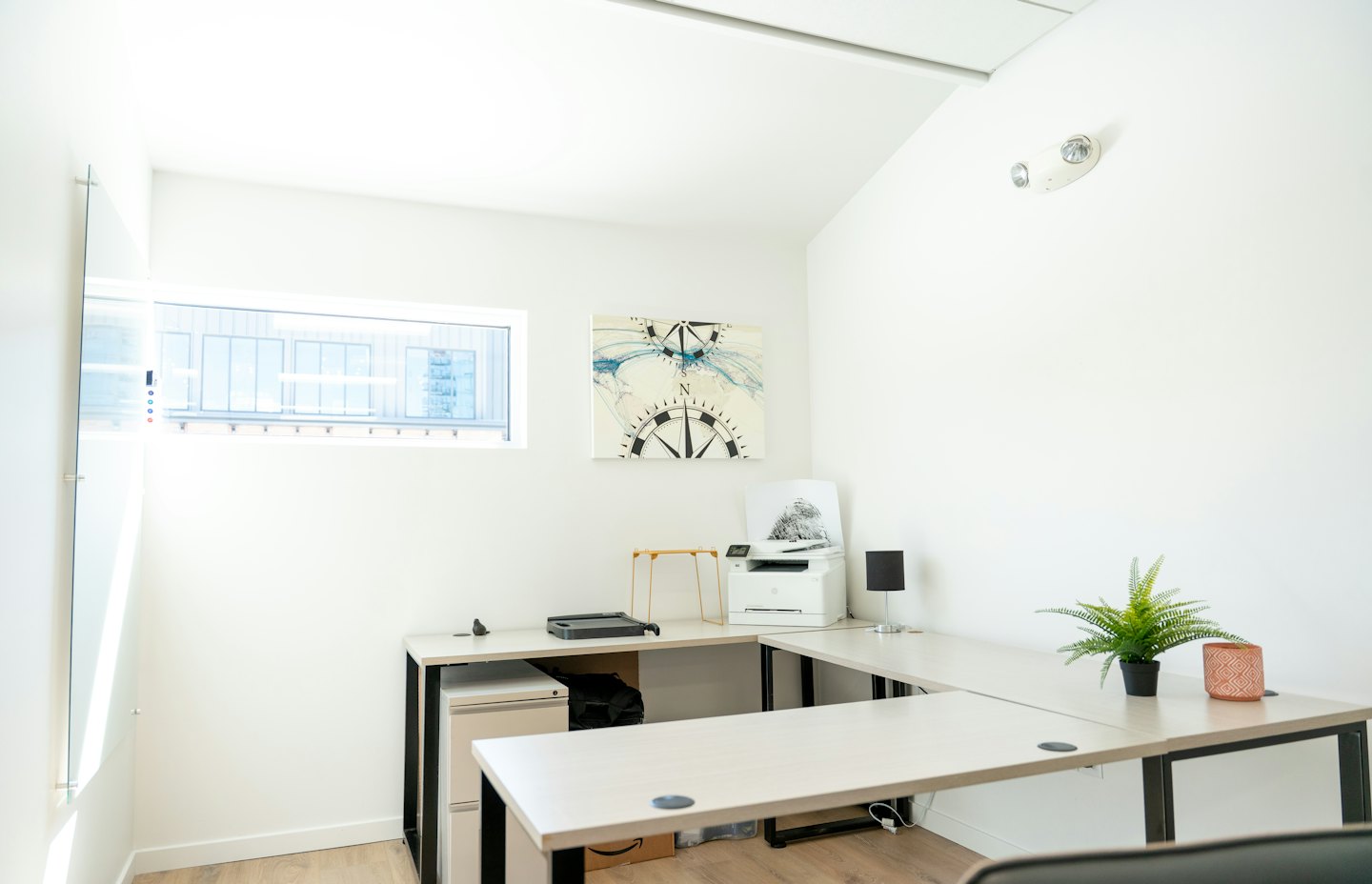 Minimalist home office with an L-shaped desk and compass artwork.