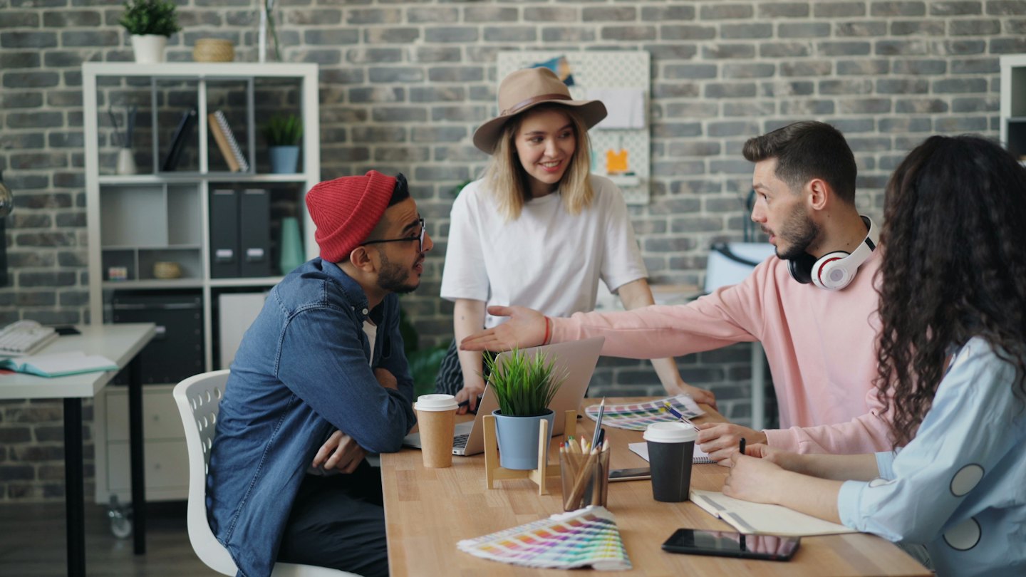 Young professionals brainstorm ideas around a table with color swatches and a laptop.